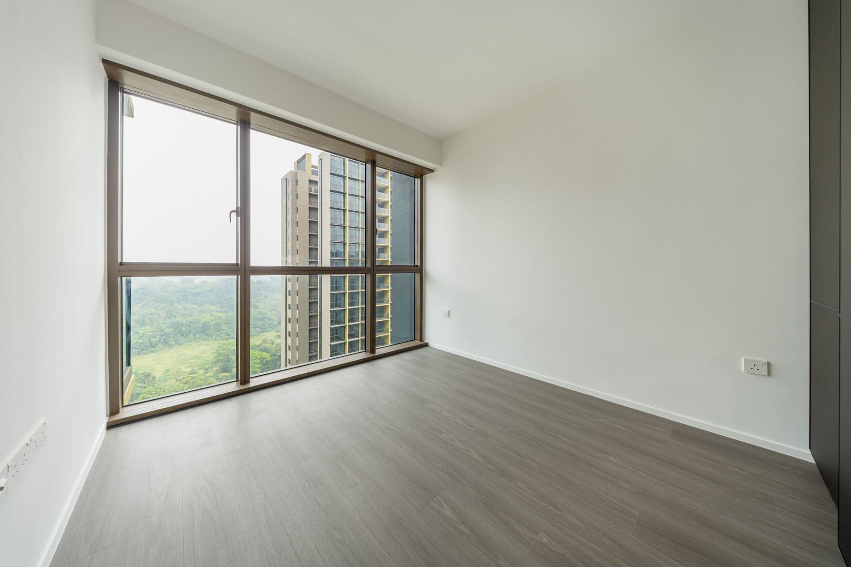 Empty bedroom with wood-look floor and a full-height window onto greenery and a neighbouring tower