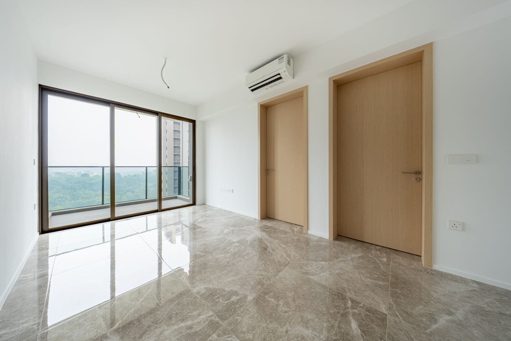 Empty living room with marble-look floor, two doors on the right and full-height glass doors to the balcony, with greenery beyond