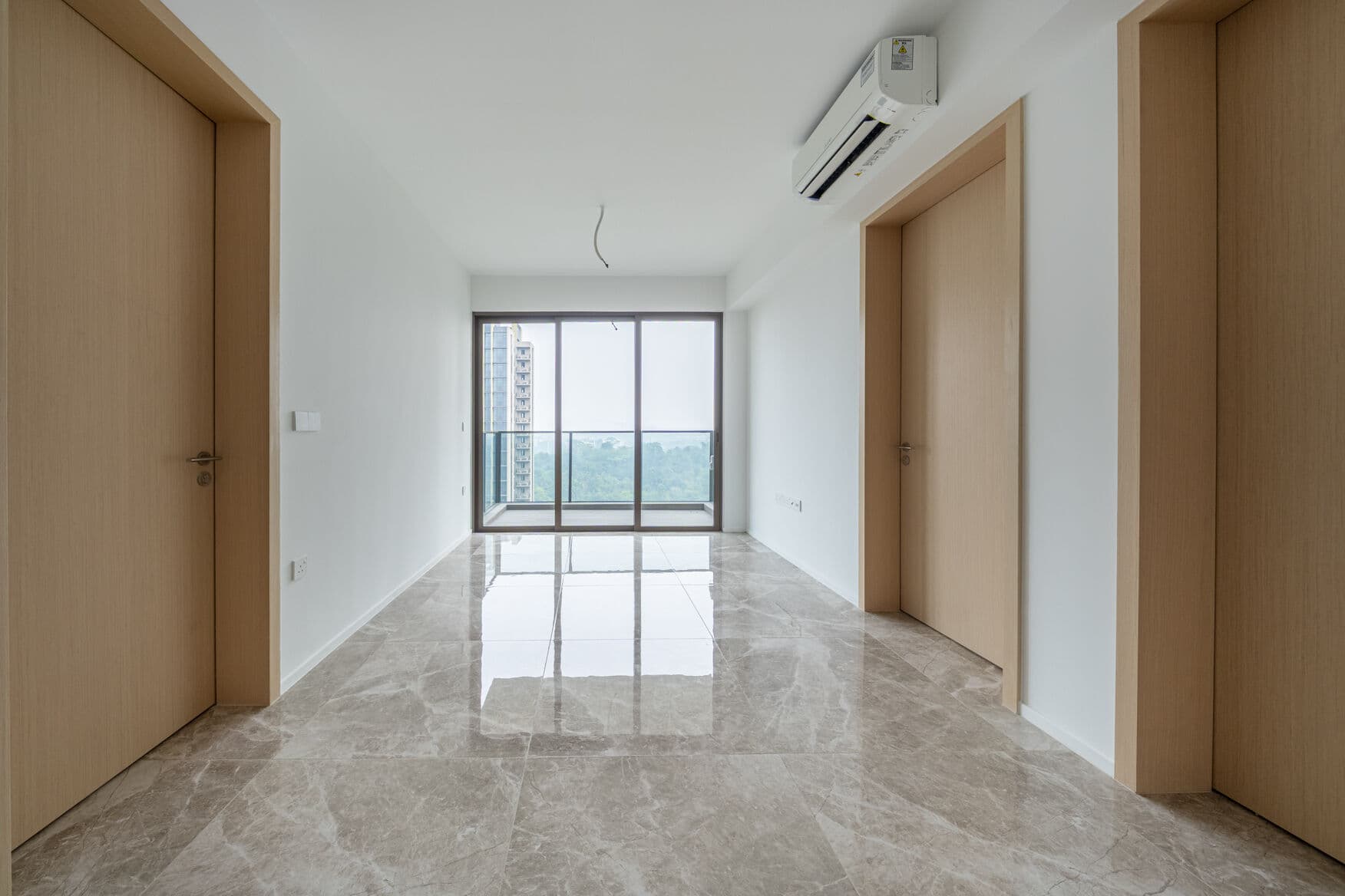 Empty living room seen from the entrance, with a bedroom door on each side and the balcony at the far end